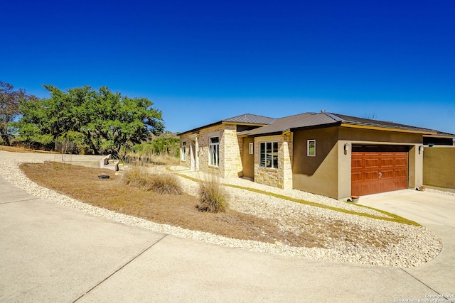 prairie-style home with stucco siding, an attached garage, a standing seam roof, metal roof, and stone siding