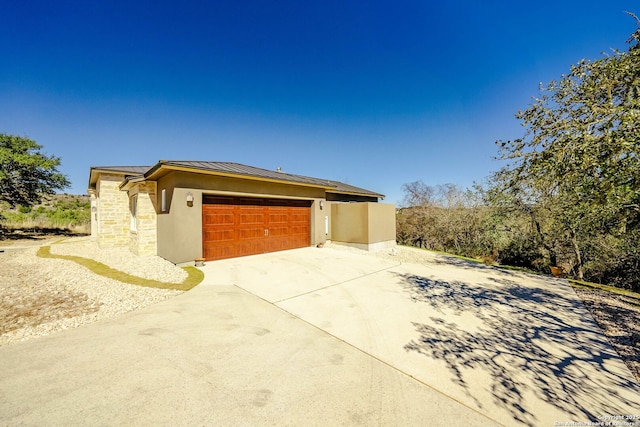 view of side of property with stucco siding, concrete driveway, a standing seam roof, metal roof, and a garage