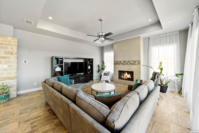 living room with visible vents, baseboards, a ceiling fan, a tray ceiling, and a fireplace