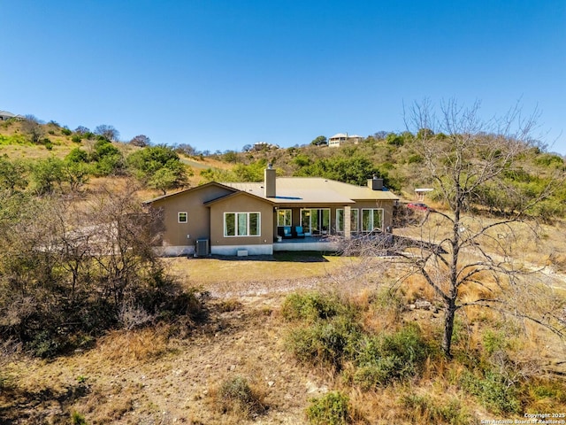 back of property with central AC unit, a chimney, and stucco siding