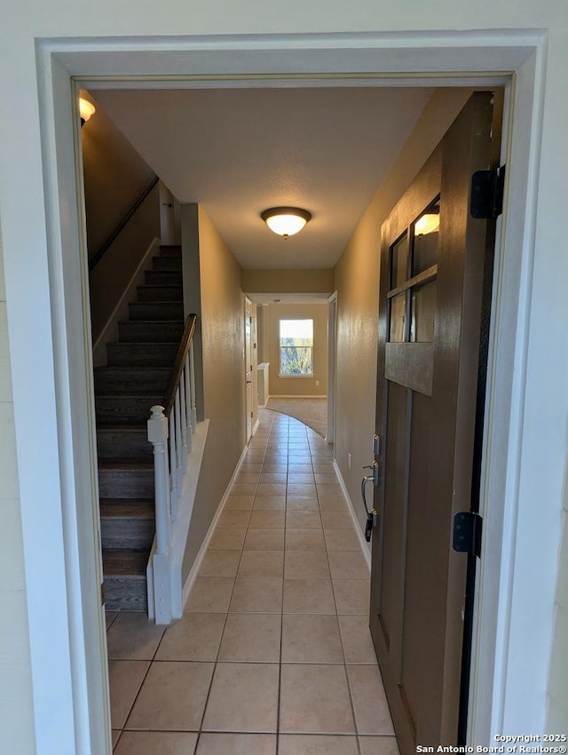 hallway featuring stairway, baseboards, and light tile patterned floors