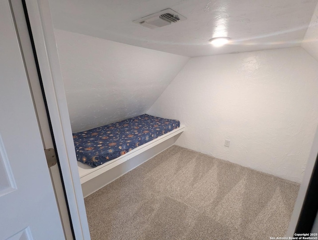 unfurnished bedroom featuring lofted ceiling, visible vents, a textured wall, and carpet flooring