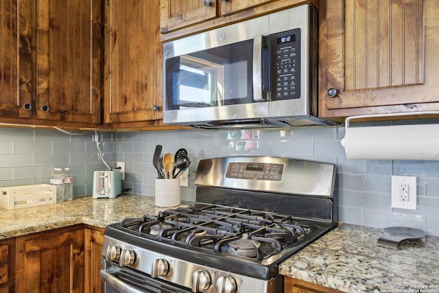 kitchen with tasteful backsplash, brown cabinets, stainless steel appliances, and light stone counters