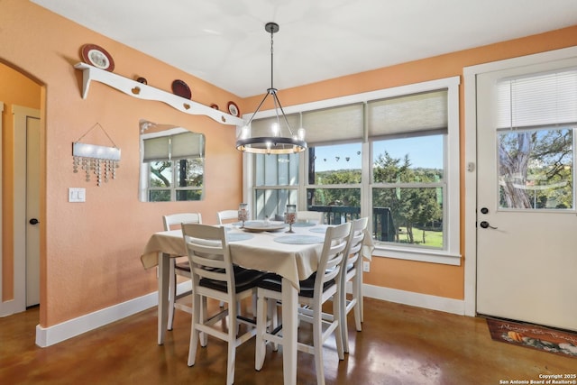 dining area with a notable chandelier, a healthy amount of sunlight, concrete floors, and baseboards