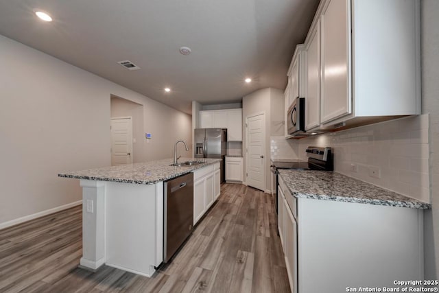 kitchen with light wood finished floors, a center island with sink, visible vents, appliances with stainless steel finishes, and a sink