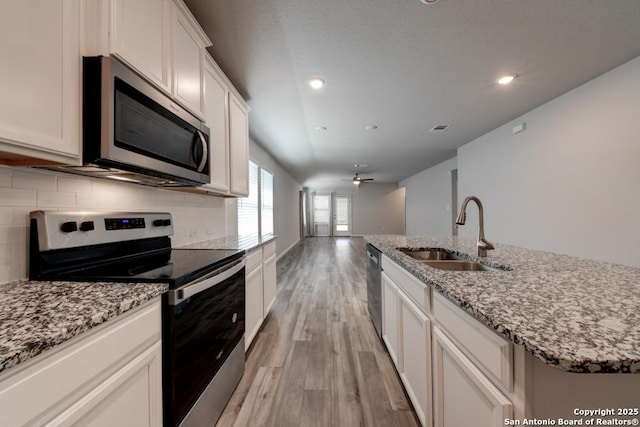 kitchen with stainless steel appliances, backsplash, light wood-style flooring, a kitchen island with sink, and a sink