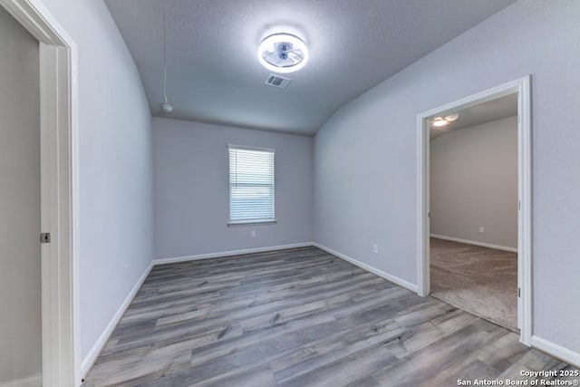 empty room featuring lofted ceiling, visible vents, baseboards, and wood finished floors