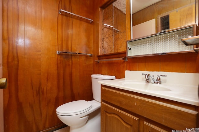 bathroom featuring toilet, wooden walls, and vanity