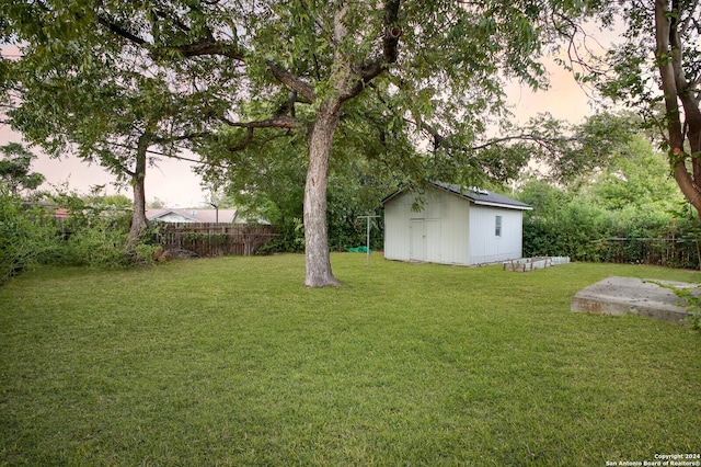 yard at dusk featuring a fenced backyard, an outdoor structure, and a storage unit