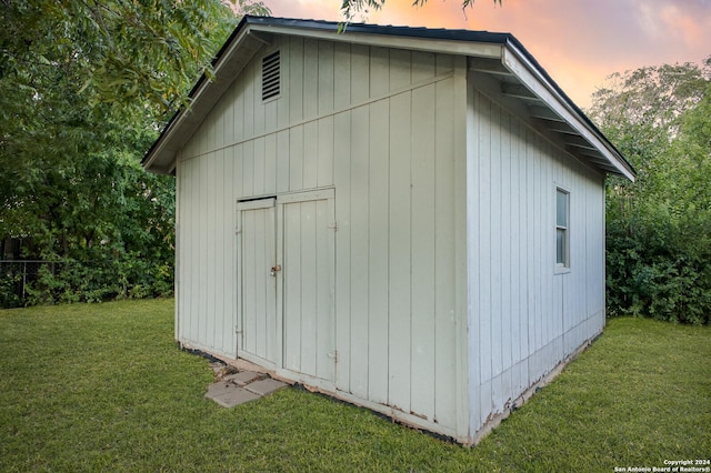 outdoor structure at dusk featuring a storage unit, a lawn, and an outdoor structure