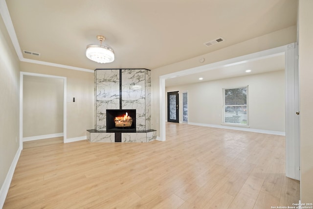 unfurnished living room featuring light wood-style floors, a high end fireplace, visible vents, and baseboards