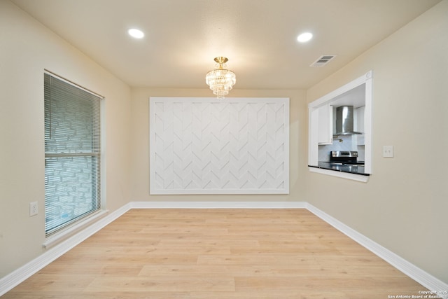 spare room featuring visible vents, a notable chandelier, light wood-style flooring, and baseboards