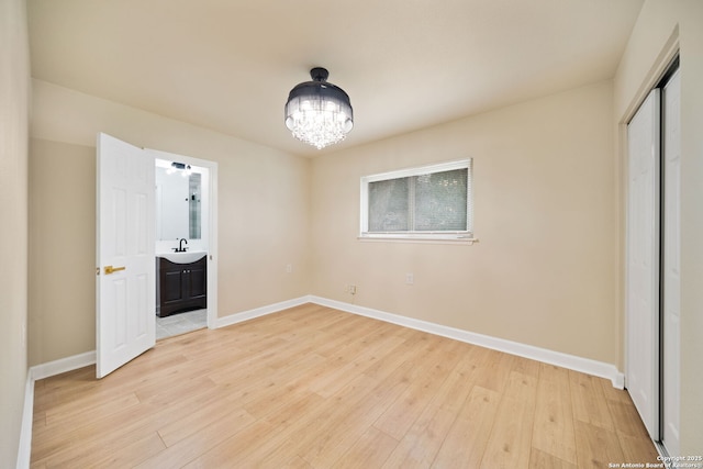 unfurnished bedroom featuring a notable chandelier, light wood finished floors, and baseboards