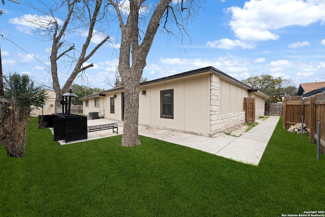 back of house featuring stone siding, a patio area, a yard, and a fenced backyard