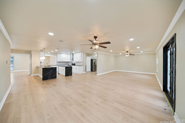 unfurnished living room with visible vents, crown molding, light wood-style flooring, and baseboards