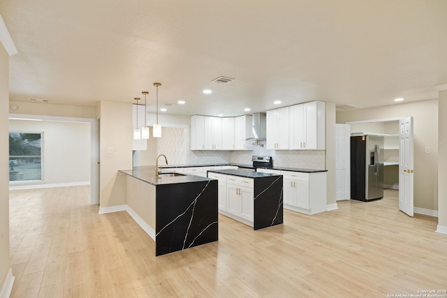 kitchen with wall chimney exhaust hood, appliances with stainless steel finishes, a peninsula, a sink, and backsplash