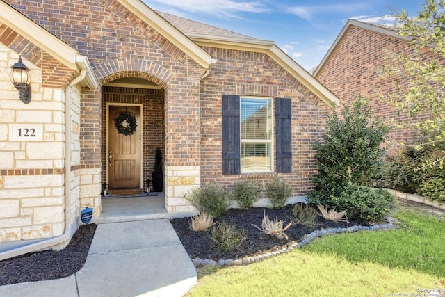 entrance to property with a shingled roof and brick siding