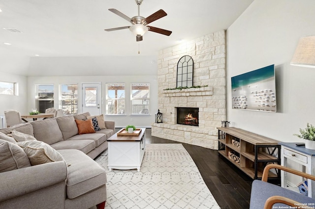 living room featuring a healthy amount of sunlight, visible vents, dark wood-style flooring, and a stone fireplace