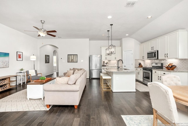 living area with visible vents, arched walkways, lofted ceiling, dark wood-style floors, and ceiling fan with notable chandelier