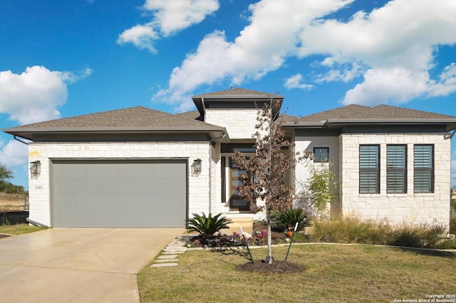 prairie-style house featuring an attached garage, a shingled roof, a front lawn, and concrete driveway