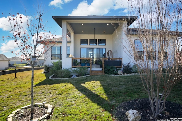 back of house with covered porch, a lawn, fence, and stucco siding