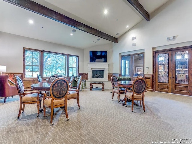 dining area with a fireplace with raised hearth, recessed lighting, a wainscoted wall, light carpet, and beam ceiling