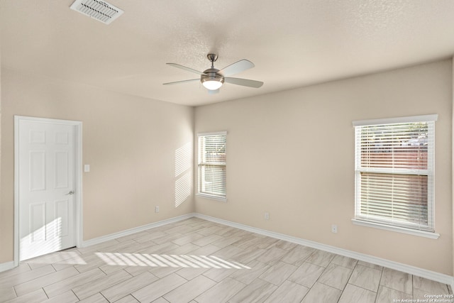 unfurnished room with a healthy amount of sunlight, ceiling fan, visible vents, and baseboards