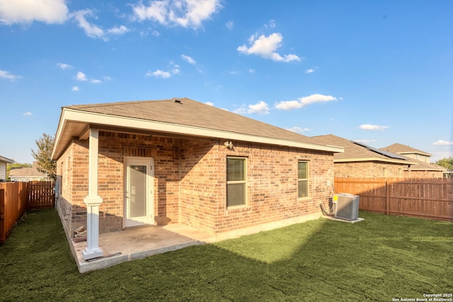 rear view of house featuring a patio, a fenced backyard, a yard, central air condition unit, and brick siding