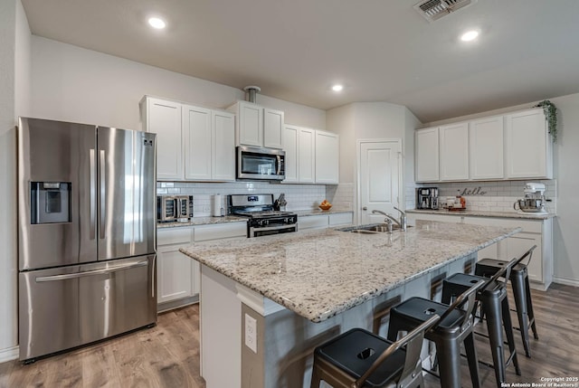 kitchen with light wood-style flooring, stainless steel appliances, a sink, visible vents, and a kitchen bar