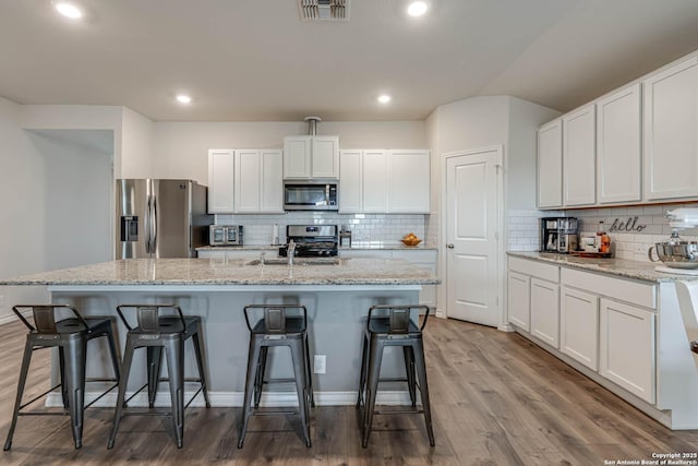 kitchen featuring a breakfast bar area, stainless steel appliances, visible vents, white cabinetry, and wood finished floors