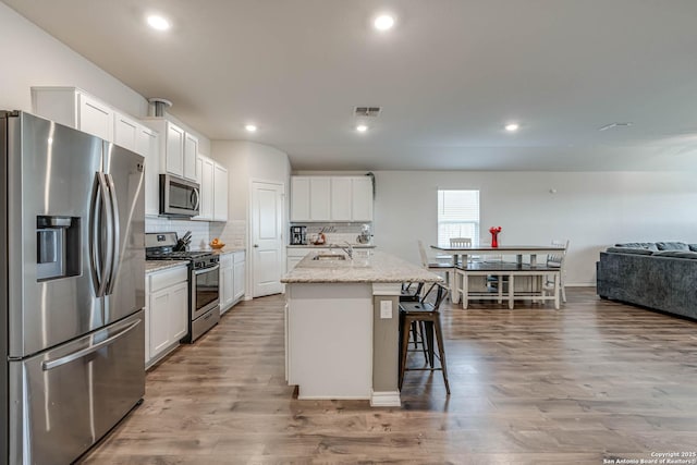 kitchen with stainless steel appliances, wood finished floors, a sink, white cabinetry, and tasteful backsplash