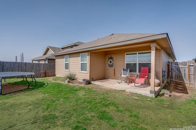 rear view of property with a yard, a fenced backyard, a patio, and a trampoline