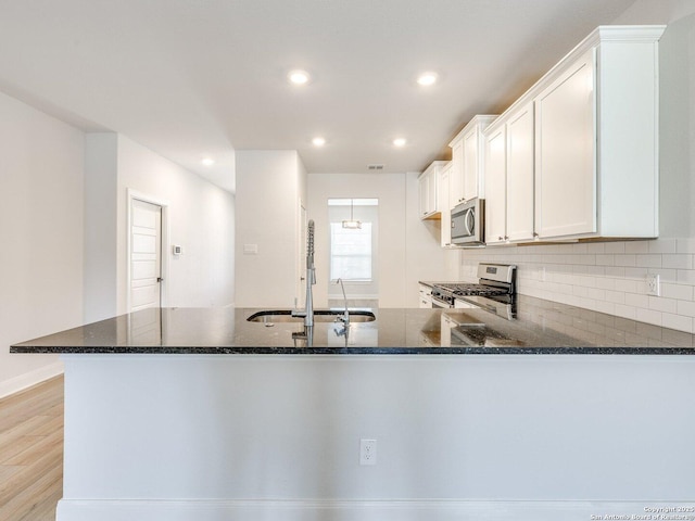 kitchen featuring white cabinets, dark stone counters, a sink, stainless steel appliances, and backsplash