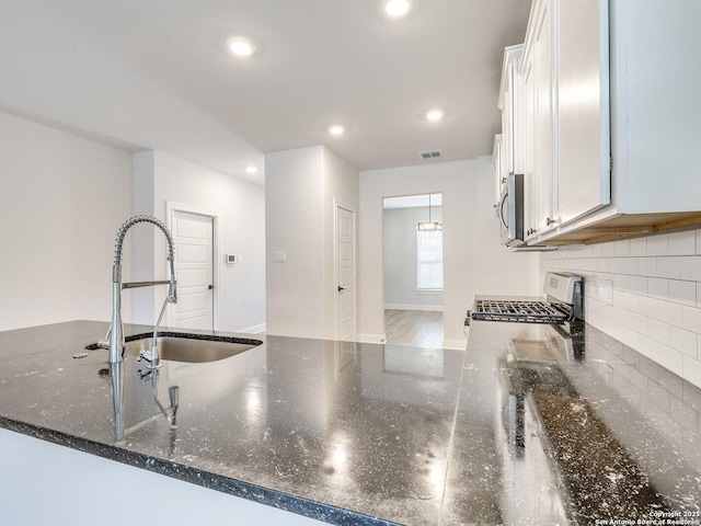 kitchen featuring white cabinets, dark stone counters, stainless steel appliances, and a sink