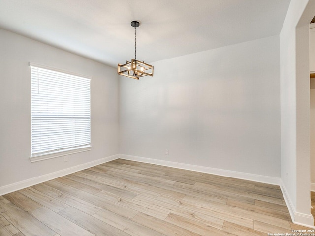 unfurnished room featuring a notable chandelier, light wood-type flooring, and baseboards