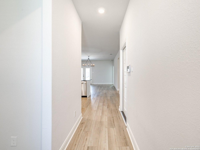 corridor with light wood-type flooring, a notable chandelier, and baseboards