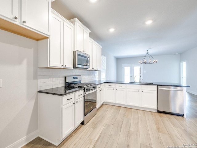 kitchen featuring a peninsula, a sink, appliances with stainless steel finishes, light wood finished floors, and dark countertops