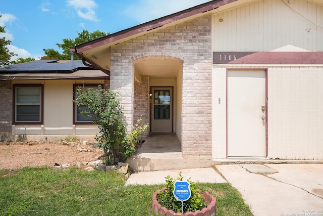 view of exterior entry featuring solar panels and brick siding