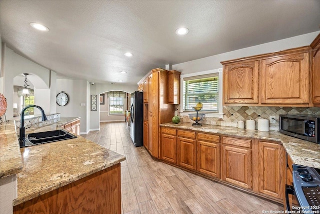 6822 Moss Oak, San Antonio, TX 78229 - kitchen with arched walkways, a sink, freestanding refrigerator, light wood-style flooring, and healthy amount of natural light