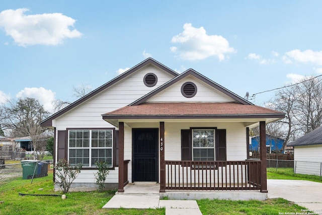 bungalow-style house with a porch, roof with shingles, a front yard, and fence