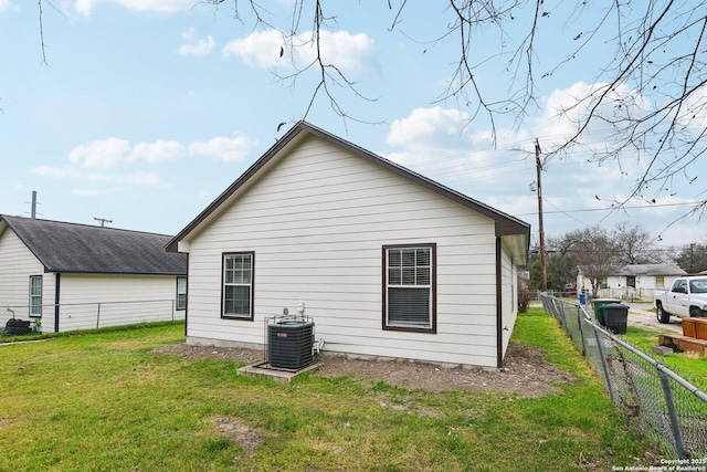 rear view of house with central air condition unit, fence, and a lawn