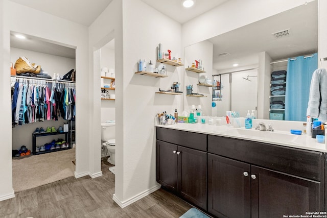 bathroom with a walk in closet, visible vents, vanity, and wood finished floors