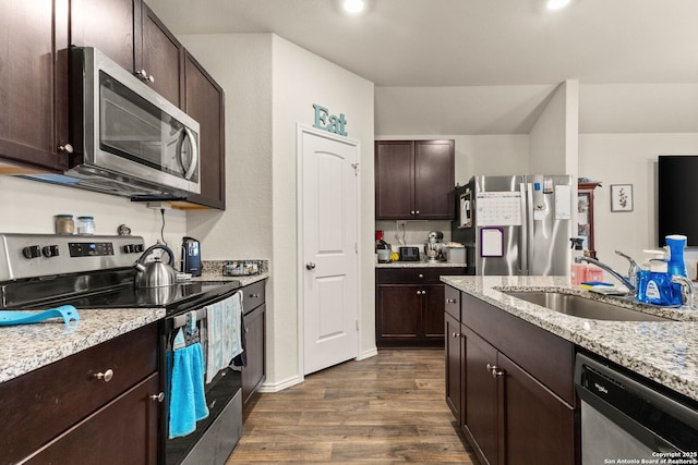 kitchen with light stone counters, a sink, dark brown cabinets, appliances with stainless steel finishes, and dark wood finished floors