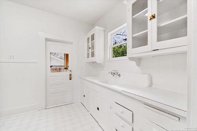 interior space featuring light floors, light countertops, glass insert cabinets, white cabinets, and a sink