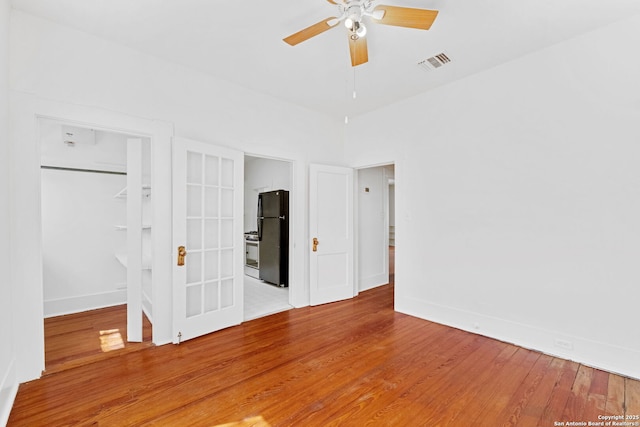 unfurnished bedroom with wood finished floors, visible vents, baseboards, a spacious closet, and freestanding refrigerator