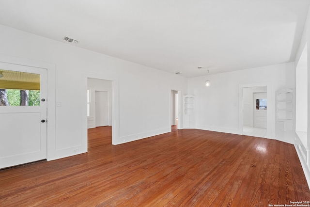 unfurnished living room featuring wood-type flooring, built in features, visible vents, and baseboards