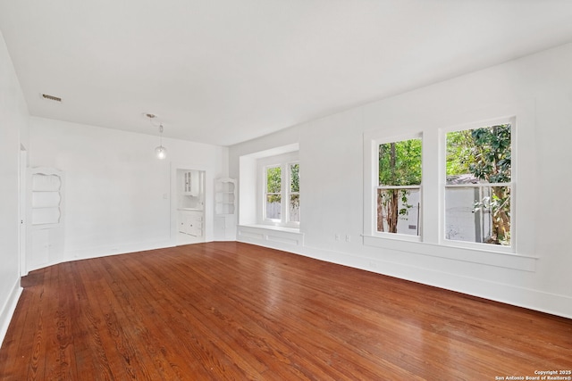 unfurnished room featuring baseboards, built in shelves, visible vents, and wood finished floors