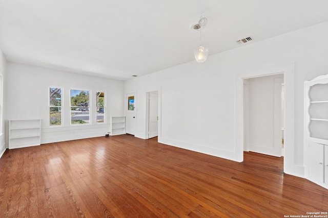 empty room featuring wood-type flooring, visible vents, and baseboards