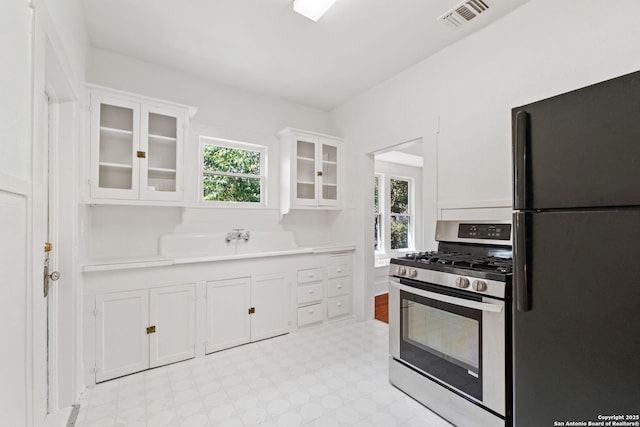 kitchen with visible vents, white cabinets, light countertops, stainless steel gas range, and freestanding refrigerator