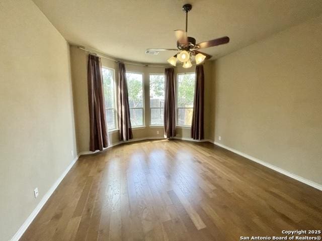 unfurnished room with ceiling fan, plenty of natural light, wood finished floors, and baseboards